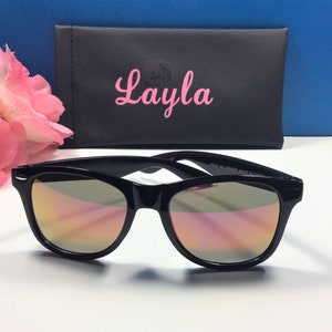 Pu&ograve; includere: Occhiali da sole neri con lenti a specchio e una custodia nera con il nome "Layla" stampato in rosa.