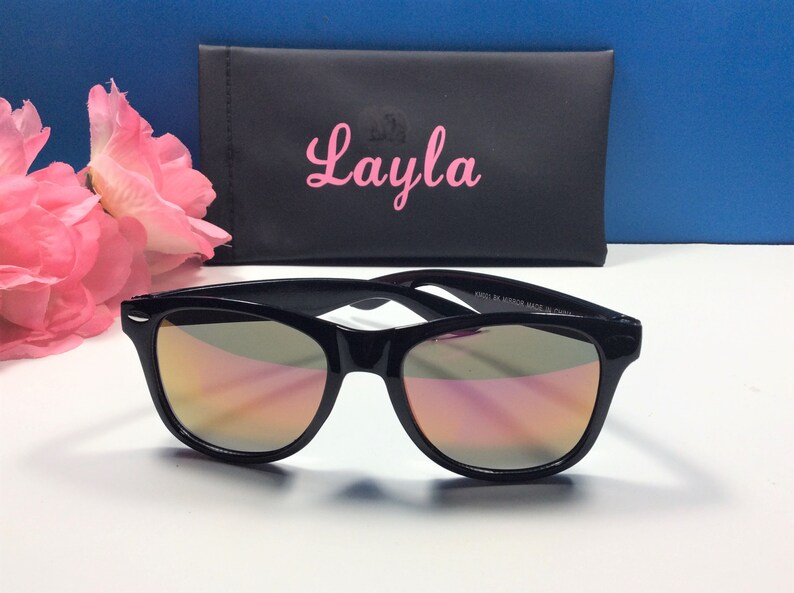 Pu&ograve; includere: Occhiali da sole neri con lenti a specchio e una custodia nera con il nome "Layla" stampato in rosa.