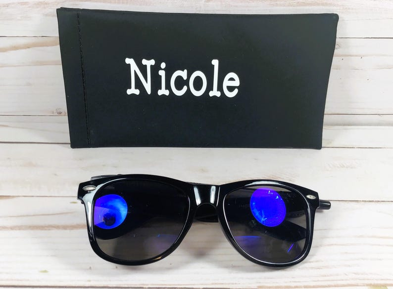 Pu&ograve; includere: Occhiali da sole neri con lenti colorate blu e una custodia nera con il nome "Nicole" stampato in bianco.