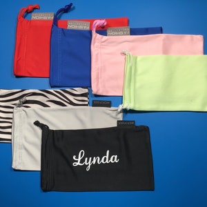 May include: Assortment of 10 colorful microfiber eyeglass cleaning cloths. The cloths are in various colors, including red, blue, pink, green, black, white, and zebra print. Some cloths have the text "MICROFIBER" and "COLLECTION FASHION" printed on them. One cloth has the name "Lynda" embroidered on it.
