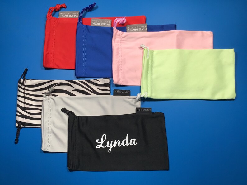 May include: Assortment of 10 colorful microfiber eyeglass cleaning cloths. The cloths are in various colors, including red, blue, pink, green, black, white, and zebra print. Some cloths have the text "MICROFIBER" and "COLLECTION FASHION" printed on them. One cloth has the name "Lynda" embroidered on it.