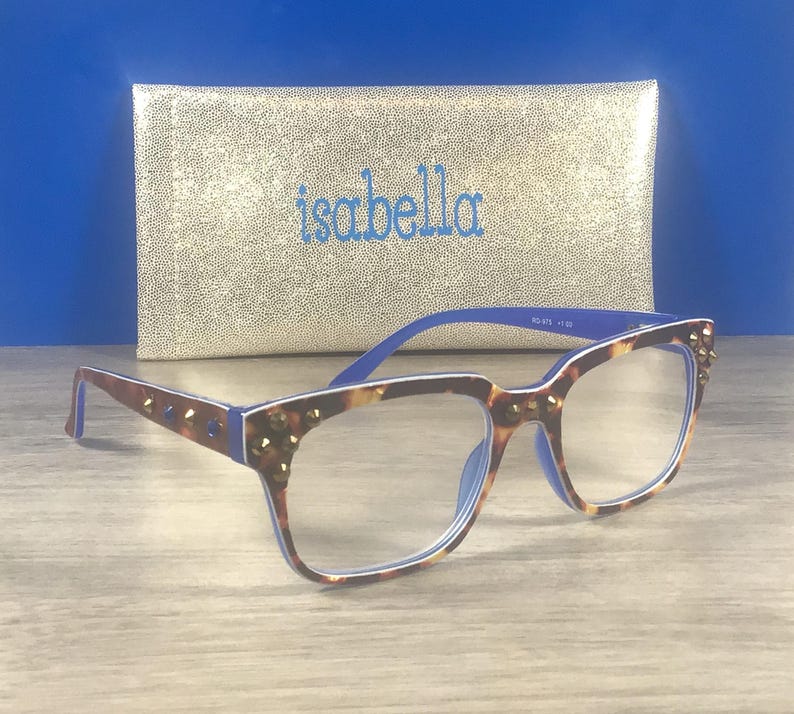 Puede incluir: Gafas de lectura con estampado de carey, detalles azules y tachuelas. Detr&aacute;s de las gafas hay un estuche dorado con el nombre "isabella" bordado en azul.
