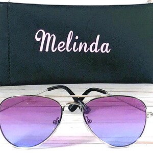 Peut inclure: Lunettes de soleil aviateur &agrave; d&eacute;grad&eacute; violet et bleu avec une monture argent&eacute;e et un &eacute;tui de transport noir avec le nom "Melinda" imprim&eacute; dessus.