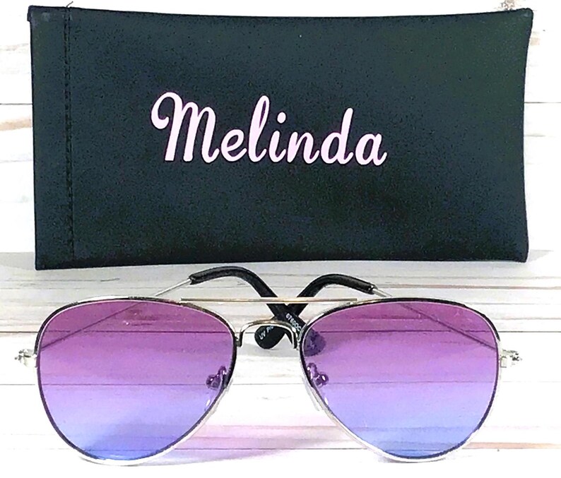 Peut inclure: Lunettes de soleil aviateur &agrave; d&eacute;grad&eacute; violet et bleu avec une monture argent&eacute;e et un &eacute;tui de transport noir avec le nom "Melinda" imprim&eacute; dessus.