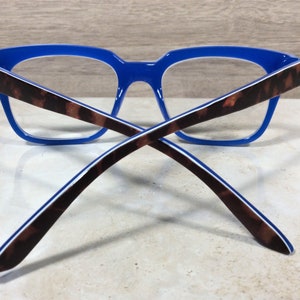 May include: Blue eyeglasses with a tortoiseshell pattern on the temples. The frames are a vibrant blue, and the arms feature a brown and black tortoiseshell design with a white stripe. The glasses are designed for vision correction.