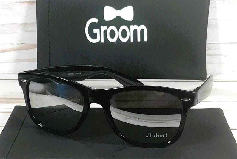 May include: Black sunglasses with a black frame and dark lenses. The sunglasses have the word "Hubert" printed on the right lens.