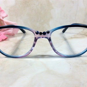 Puede incluir: Gafas de estilo ojo de gato con montura degradada azul y morada. La montura est&aacute; adornada con pedrer&iacute;a azul oscuro en las esquinas y el puente. Las gafas tienen lentes transparentes y varillas negras.