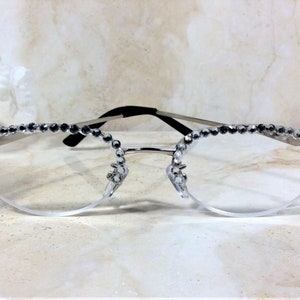 Pu&ograve; includere: Occhiali con montatura argentata e lenti trasparenti, adornati con strass scintillanti lungo il bordo superiore e sulle aste. Gli occhiali hanno un design delicato ed elegante, perfetto per aggiungere un tocco di glamour. La montatura &egrave; argentata con aste nere.