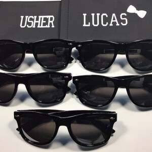 May include: Four pairs of black sunglasses with dark lenses. The sunglasses are arranged in two rows of two. The top row has the words "USHER" and "LUCAS" on the boxes behind them.