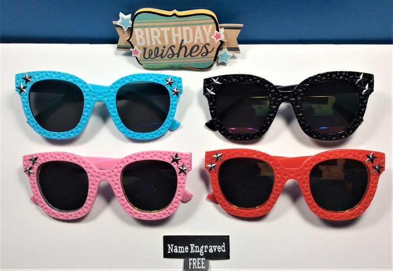 Puede incluir: Cuatro pares de gafas de sol con detalles de estrellas. Las gafas de sol son de color azul, negro, rosa y rojo. El texto "Birthday Wishes" es visible sobre las gafas de sol.