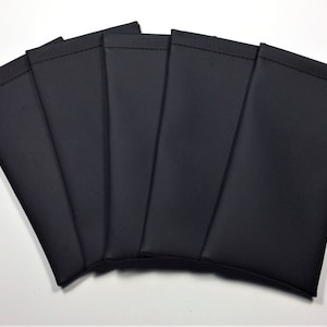 May include: A collection of six black, rectangular pouches, possibly for glasses or small electronics, are fanned out against a white background. Each pouch is made of a smooth, dark material with a stitched top edge.