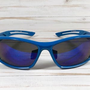 May include: Blue sport sunglasses with dark lenses. The sunglasses have a wraparound design and a thick frame. The text "ESTWAY CHINA" is printed on the left arm and "UV Protection" on the right arm.