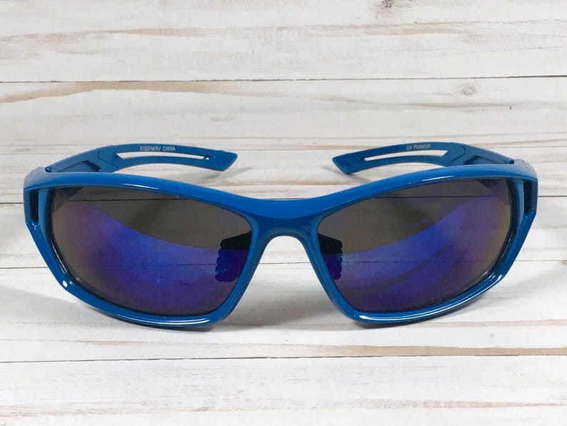 May include: Blue sport sunglasses with dark lenses. The sunglasses have a wraparound design and a thick frame. The text "ESTWAY CHINA" is printed on the left arm and "UV Protection" on the right arm.