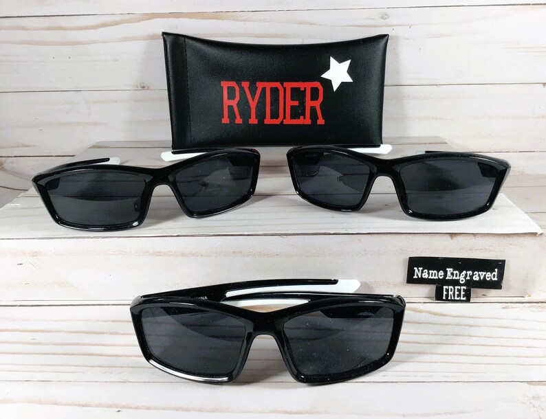 May include: Two pairs of black sunglasses with white accents and a black case with the word "RYDER" in red letters and a white star. The case also has the text "Name Engraved FREE".