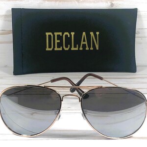 Pode incluir: &Oacute;culos de sol aviador dourados com lentes cinza escuras e uma caixa preta com a palavra "DECL&Aacute;N" impressa em letras douradas.