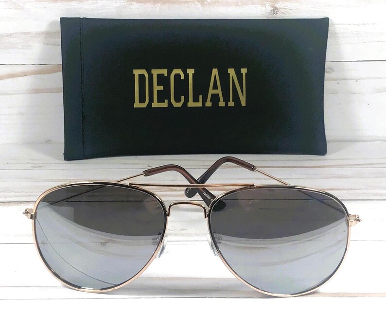 Pode incluir: &Oacute;culos de sol aviador dourados com lentes cinza escuras e uma caixa preta com a palavra "DECL&Aacute;N" impressa em letras douradas.