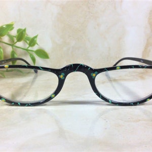 K&ouml;nnte beinhalten: Schwarz gerahmte Lesebrille mit floralem Design in T&uuml;rkis und Gelb. Die Fassungen sind mit gr&uuml;nen Strasssteinen an den Ecken verziert. Die Brille hat ein Halbrahmen-Design.
