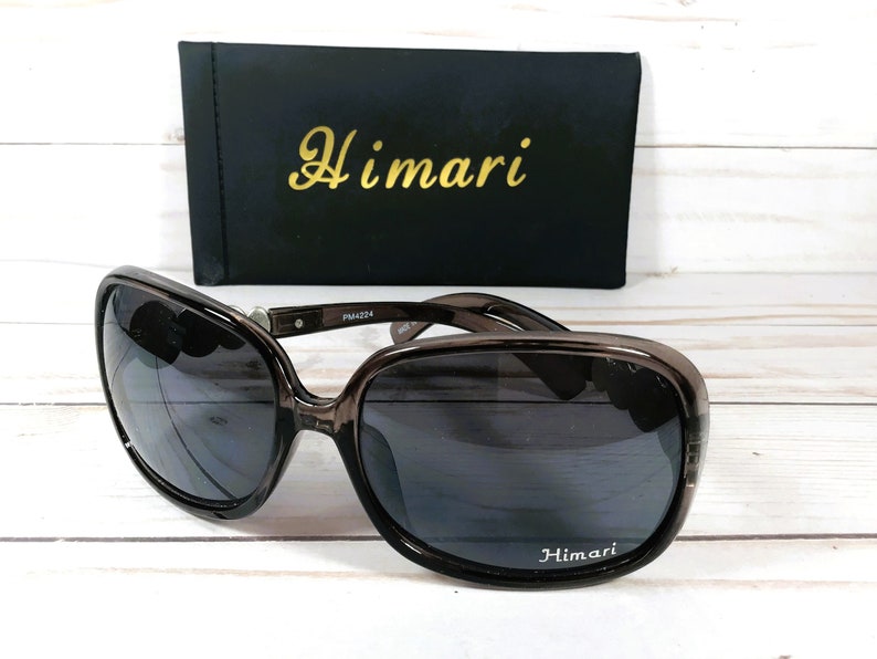 Puede incluir: Gafas de sol de pl&aacute;stico marr&oacute;n con lentes oscuros. Las gafas tienen la palabra "Himari" impresa en la lente derecha y la caja tiene la palabra "Himari" impresa en la parte delantera.