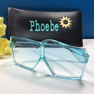 May include: Light blue square-shaped sunglasses with a black case that says "Phoebe" and has a yellow sun graphic.