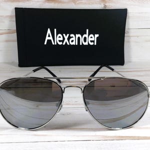 May include: Silver aviator sunglasses with mirrored lenses and a black case with the word "Alexander" printed on it.