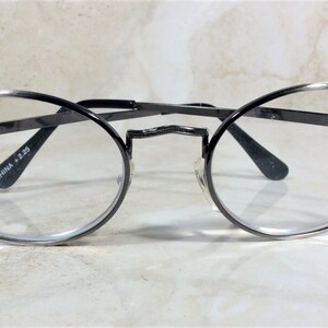 Puede incluir: Gafas ovaladas con montura de metal gris oscuro. Las patillas est&aacute;n adornadas con peque&ntilde;os brillantes rosas. Las lentes son transparentes y el texto "CHINA +2.25" est&aacute; impreso en la patilla.