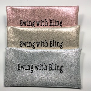 Pu&ograve; includere: Tre pochette metalliche impilate, rosa, oro e argento. Ogni pochette ha una texture puntinata e la scritta "Swing with Bling" in nero.