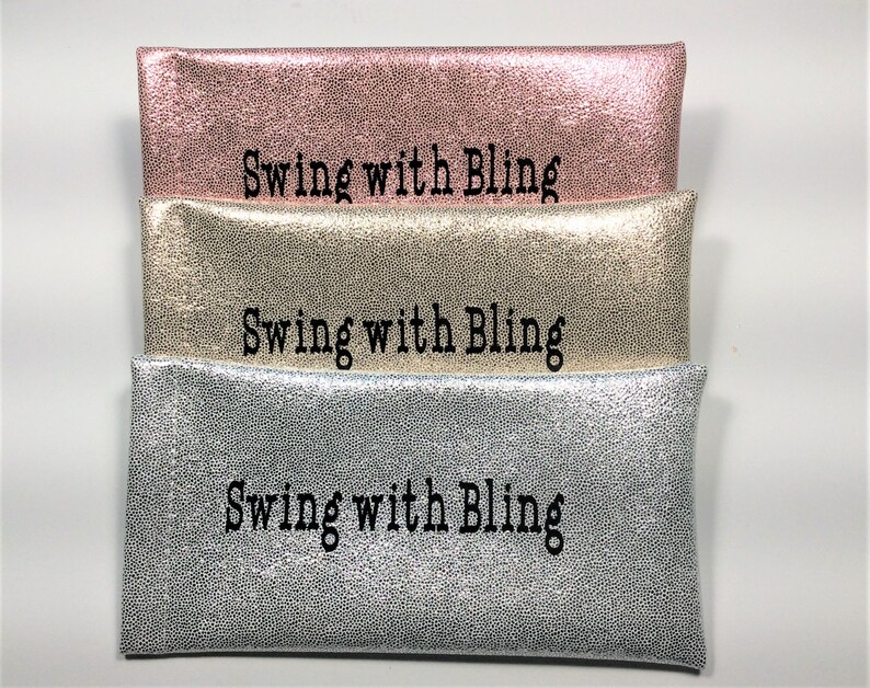 Pu&ograve; includere: Tre pochette metalliche impilate, rosa, oro e argento. Ogni pochette ha una texture puntinata e la scritta "Swing with Bling" in nero.