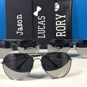 Może przedstawiać: Trzy pary srebrnych okular&oacute;w przeciwsłonecznych typu aviator z lustrzanymi szkłami. Okulary są ułożone w rzędzie, najmniejsze z przodu, a największe z tyłu. Okulary są ostre, a tło rozmyte.