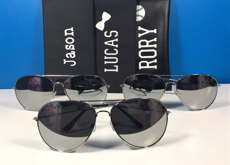 Może przedstawiać: Trzy pary srebrnych okular&oacute;w przeciwsłonecznych typu aviator z lustrzanymi szkłami. Okulary są ułożone w rzędzie, najmniejsze z przodu, a największe z tyłu. Okulary są ostre, a tło rozmyte.
