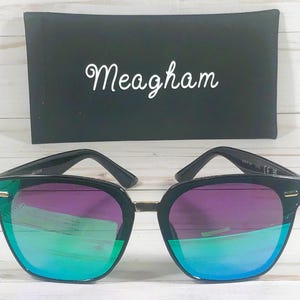 May include: Black sunglasses with a green and purple mirrored lens. The sunglasses have a gold accent on the frame.