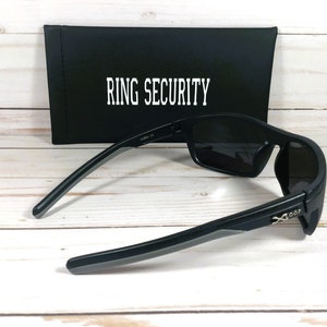 Peut inclure: Lunettes de soleil noires avec des verres fonc&eacute;s et un &eacute;tui noir. L'&eacute;tui porte l'inscription "RING SECURITY" en blanc. Les lunettes ont un design &eacute;l&eacute;gant et moderne avec une finition mate et des accents gris sur les branches.