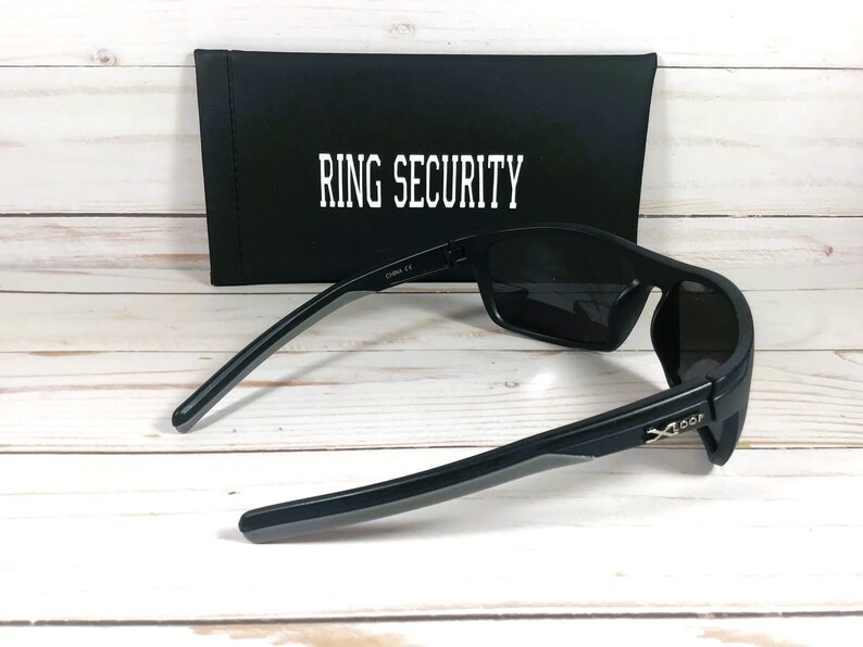 Peut inclure: Lunettes de soleil noires avec des verres fonc&eacute;s et un &eacute;tui noir. L'&eacute;tui porte l'inscription "RING SECURITY" en blanc. Les lunettes ont un design &eacute;l&eacute;gant et moderne avec une finition mate et des accents gris sur les branches.