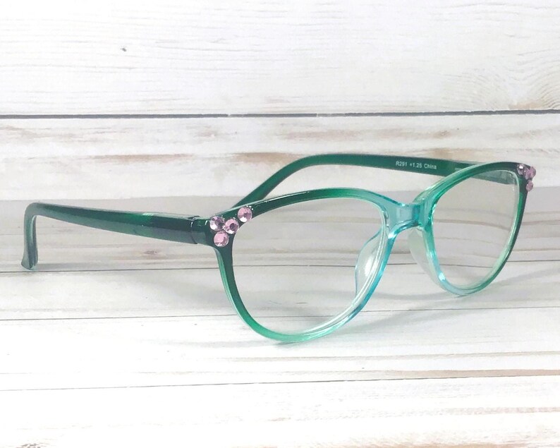 May include: Green gradient eyeglasses featuring a translucent frame that transitions from a dark forest green at the temples to a lighter mint green at the bottom. The outer corners are embellished with small, round, light pink decorative crystals.