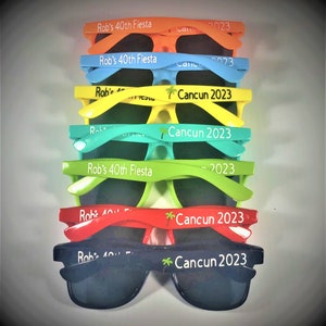 Puede incluir: Una pila de gafas de sol de colores con el texto "Rob's 40th Fiesta" y "Cancun 2023" impreso en las monturas.