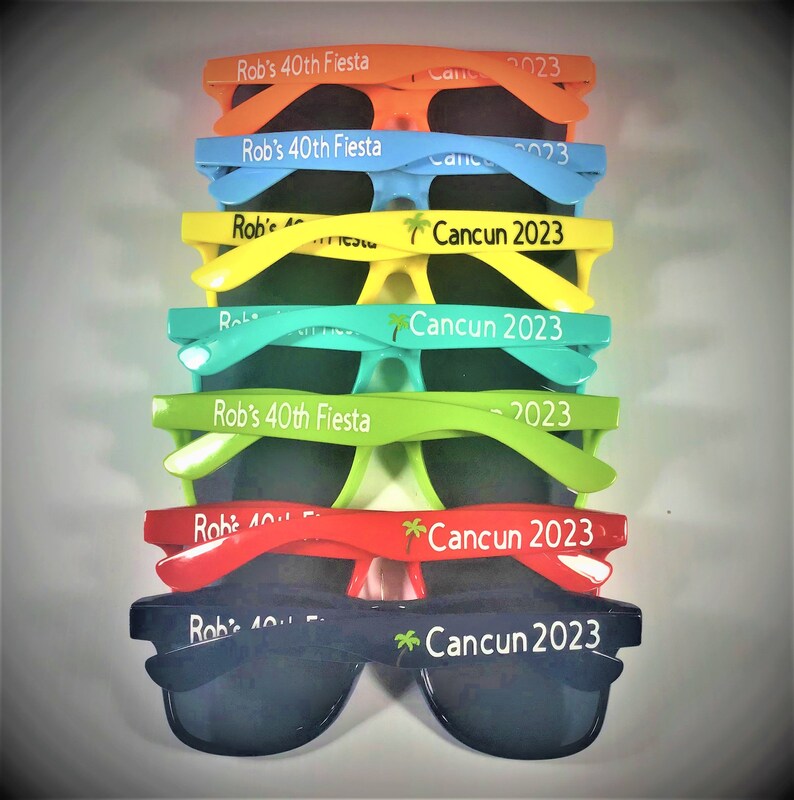 Puede incluir: Una pila de gafas de sol de colores con el texto "Rob's 40th Fiesta" y "Cancun 2023" impreso en las monturas.