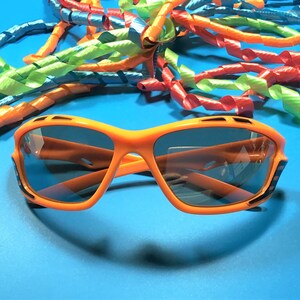 May include: Orange sunglasses with black accents and dark lenses. The sunglasses are on a blue background with colorful curly ribbons.