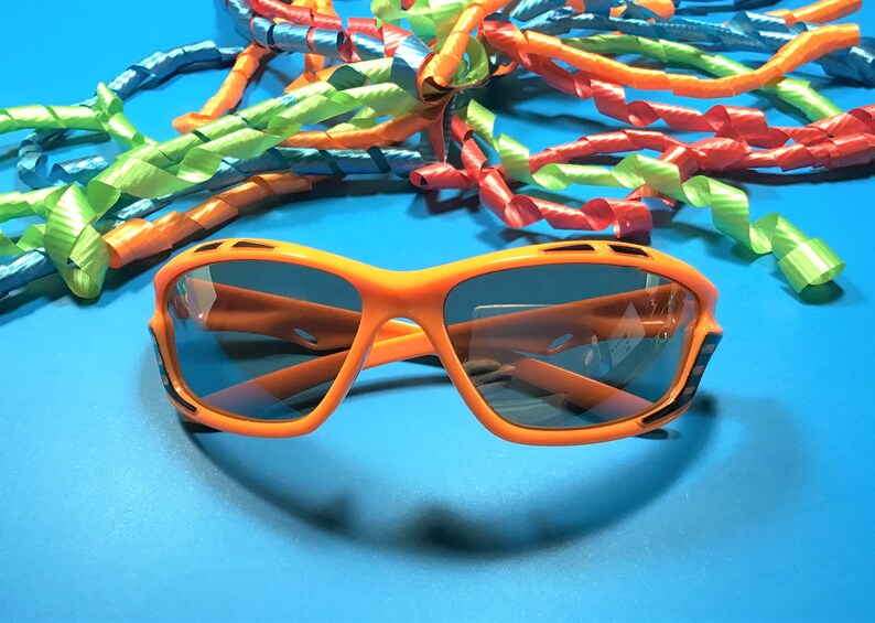 May include: Orange sunglasses with black accents and dark lenses. The sunglasses are on a blue background with colorful curly ribbons.