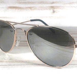 May include: Aviator sunglasses featuring a thin rose gold metal frame and a double bridge design. The lenses are dark, reflective, and teardrop-shaped. The temples have dark tips, and the nose pads are clear, providing a classic look.