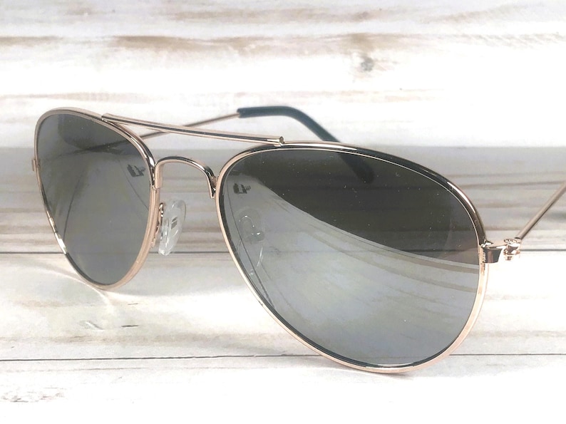 May include: Aviator sunglasses featuring a thin rose gold metal frame and a double bridge design. The lenses are dark, reflective, and teardrop-shaped. The temples have dark tips, and the nose pads are clear, providing a classic look.