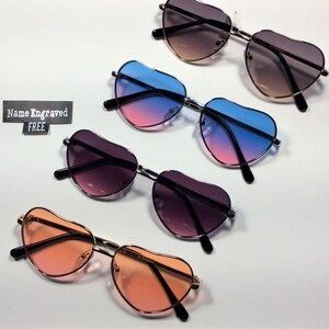 May include: Four pairs of heart-shaped sunglasses with different colored lenses. The lenses are pink and blue, pink and purple, brown and black, and orange. The text "Name Engraved FREE" is visible in the image.