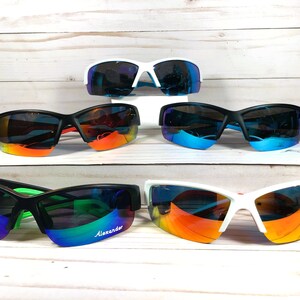 May include: Five pairs of athletic sunglasses with wrap-around frames and reflective lenses. The collection includes white and black frames with various lens colours, including blue, orange, and green. One pair features the word Alexander on the lens.