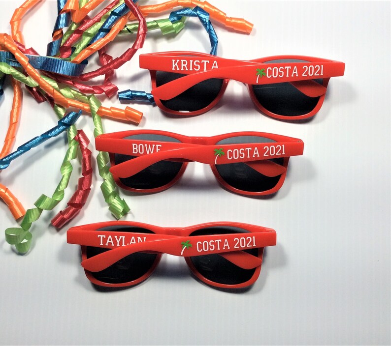 Puede incluir: Tres pares de gafas de sol de pl&aacute;stico rojo con lentes negros. Cada par tiene un nombre diferente impreso en la montura: Krista, Bowf y Taylan. Las gafas de sol tambi&eacute;n tienen el texto "COSTA 2021" impreso en la montura.