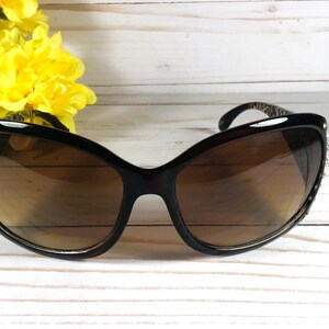 K&ouml;nnte beinhalten: Schwarze Cat-Eye-Sonnenbrille mit braunen Gl&auml;sern und Strasssteinen am Rahmen.