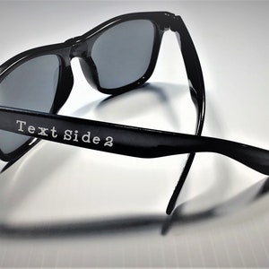 May include: Black sunglasses with a silver accent on the side. The sunglasses are folded in half and the text "Text Side 2" is engraved on the side.