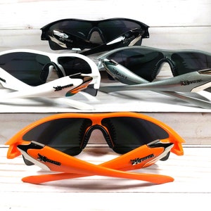 May include: Three pairs of sunglasses with different colored frames: white, silver, and orange. All sunglasses have black lenses and a similar design with a curved frame and a logo on the side.