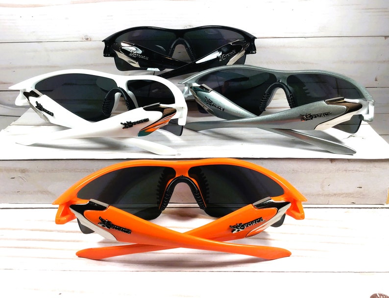 May include: Three pairs of sunglasses with different colored frames: white, silver, and orange. All sunglasses have black lenses and a similar design with a curved frame and a logo on the side.