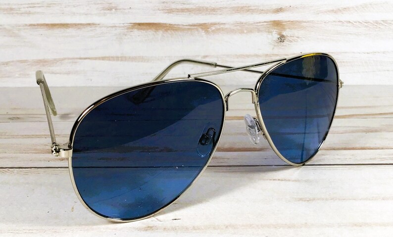 May include: Aviator sunglasses featuring a silver frame and gradient blue lenses. The lenses transition from a darker blue at the top to a lighter shade at the bottom. The sunglasses are set against a light wood grain background.