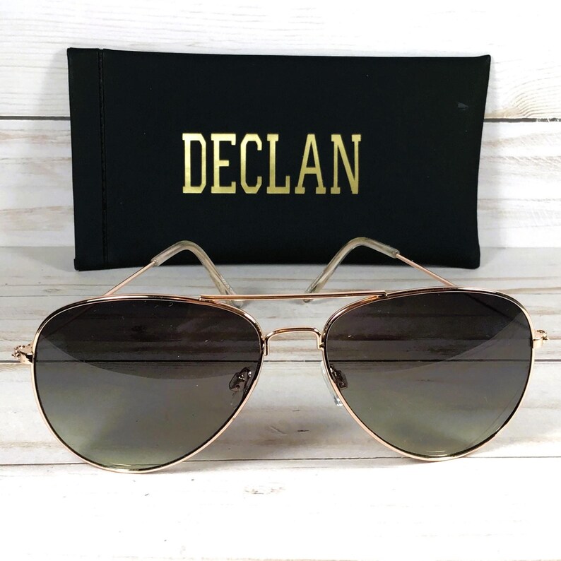 May include: Rose gold aviator sunglasses with gradient lenses. The sunglasses are paired with a black case with the name "DECLAN" in gold lettering.