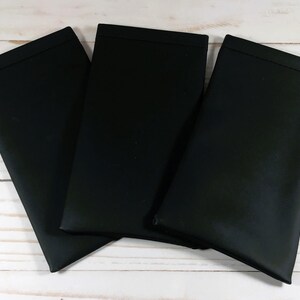 K&ouml;nnte beinhalten: Drei schwarze Stoff-Platzsets, gefaltet und &uuml;bereinander gestapelt auf einer wei&szlig;en Holzoberfl&auml;che.