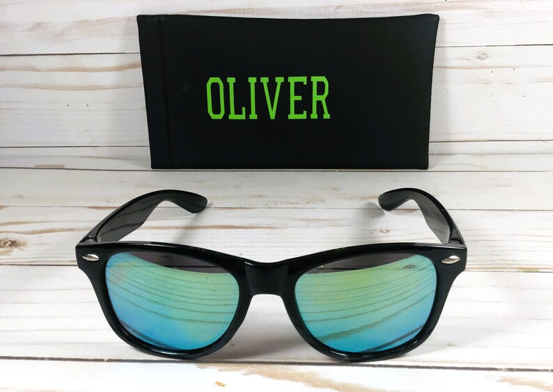 Pu&ograve; includere: Occhiali da sole neri con lenti a specchio verdi e una custodia nera con il nome "OLIVER" stampato in verde.